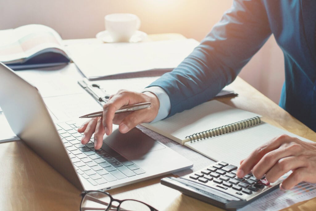 A man sitting at a laptop with calculator to illustrate new fees for Stripe and Visa concerning chargeback disputes